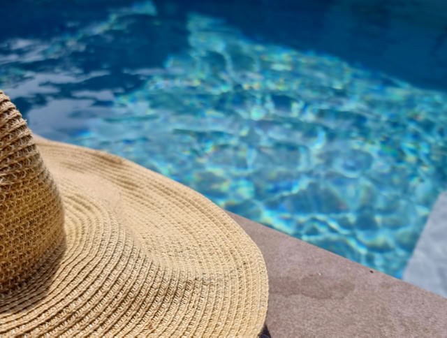 Strohhut liegt auf einem Steinrand neben einem Pool mit blauem Wasser.