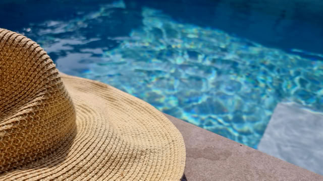 Strohhut liegt auf einem Steinrand neben einem Pool mit blauem Wasser.