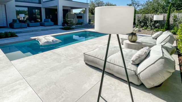 Moderne Terrasse mit Pool, Liegestühlen und Stehlampe, im Hintergrund ein Haus.